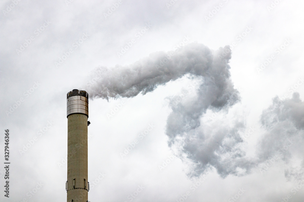Tall chimney emitting gases into the atmosphere, causing air pollution. Gray, cloudy sky.