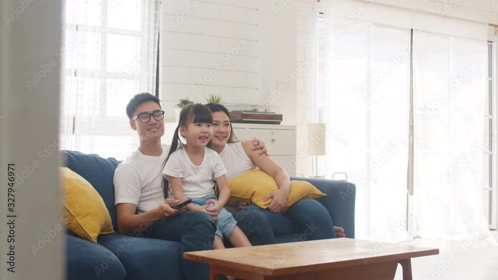 Happy Asian family enjoy their free time relax together at home. Lifestyle Korean dad, mom and daughter watching TV together and having fun lying on sofa in living room in modern house. Happy Asian family enjoy their free time relax together at home. Lifestyle Korean dad, mom and daughter watching TV together and having fun lying on sofa in living room in modern house.