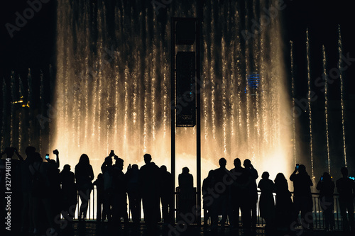 Dubai fountain with silhouettes of people on foreground at night. Popular tourist place, UAE.