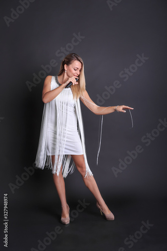 Girl with a microphone in a white dress in a photo studio on a black background