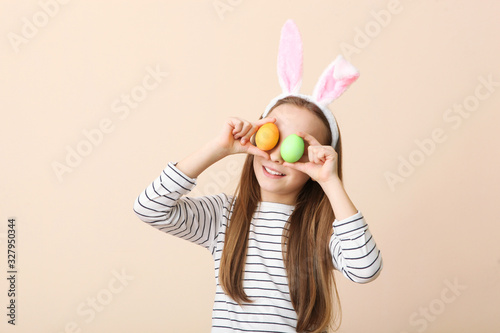Portrait of a little cute smiling girl with bunny ears and easter eggs in hands on a colored background. Easter background with place to insert text.