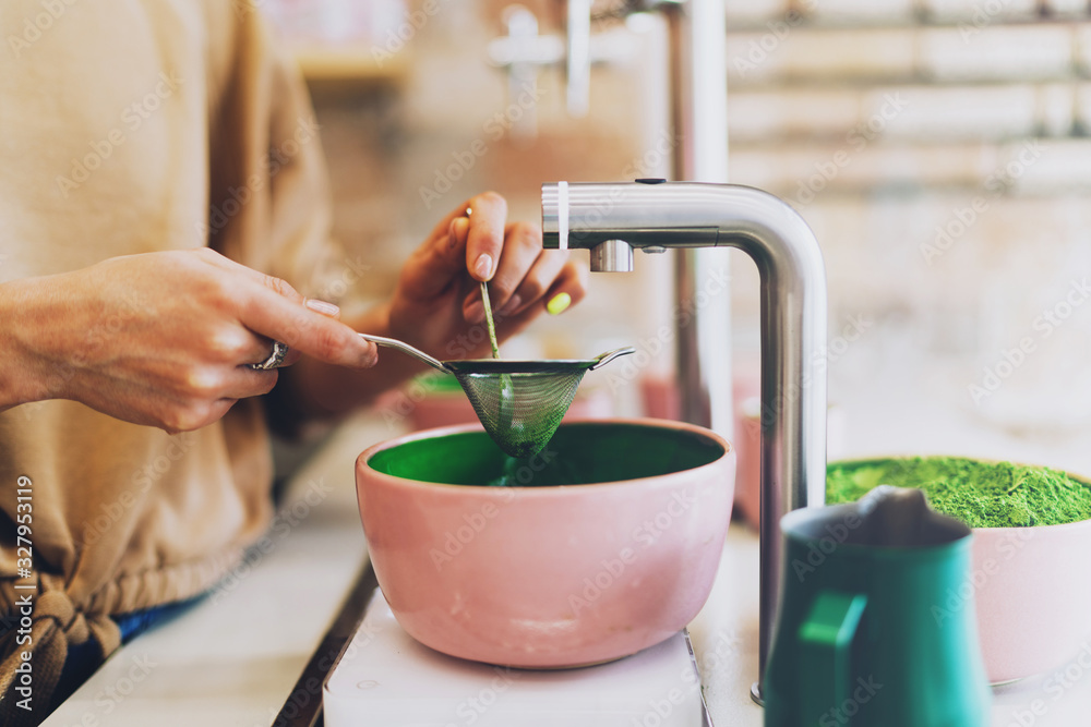 Fototapeta Professional barista making japanese matcha tea using natural ingredients and modern teaware tools. Woman's hands operating with a strainer and spoon while sieving matcha powder in a coffee shop.