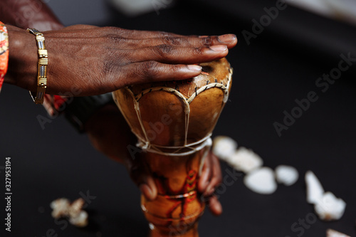 Hands of an African man in national clothes holds djembe drum surrounded by seashells © lightscience