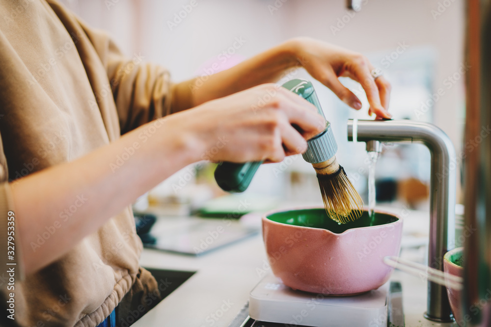 Fototapeta Process of making traditional japanese matcha tea. Barista adding water in a bowl for the matcha tea. Female's hand holding modern electric whisk for whipping the matcha powder in coffee shop.