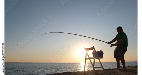 A plump man catches fish in the sea early in the morning.