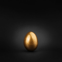Golden painted egg on black background