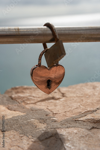 Heart shaped, vintage love padlock on steel rail. Ocean in the background. 