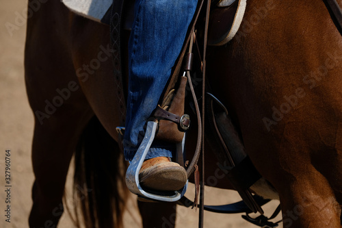 Western lifestyle shows close up of cowboy boot in aluminum stirrup while horseback riding. photo
