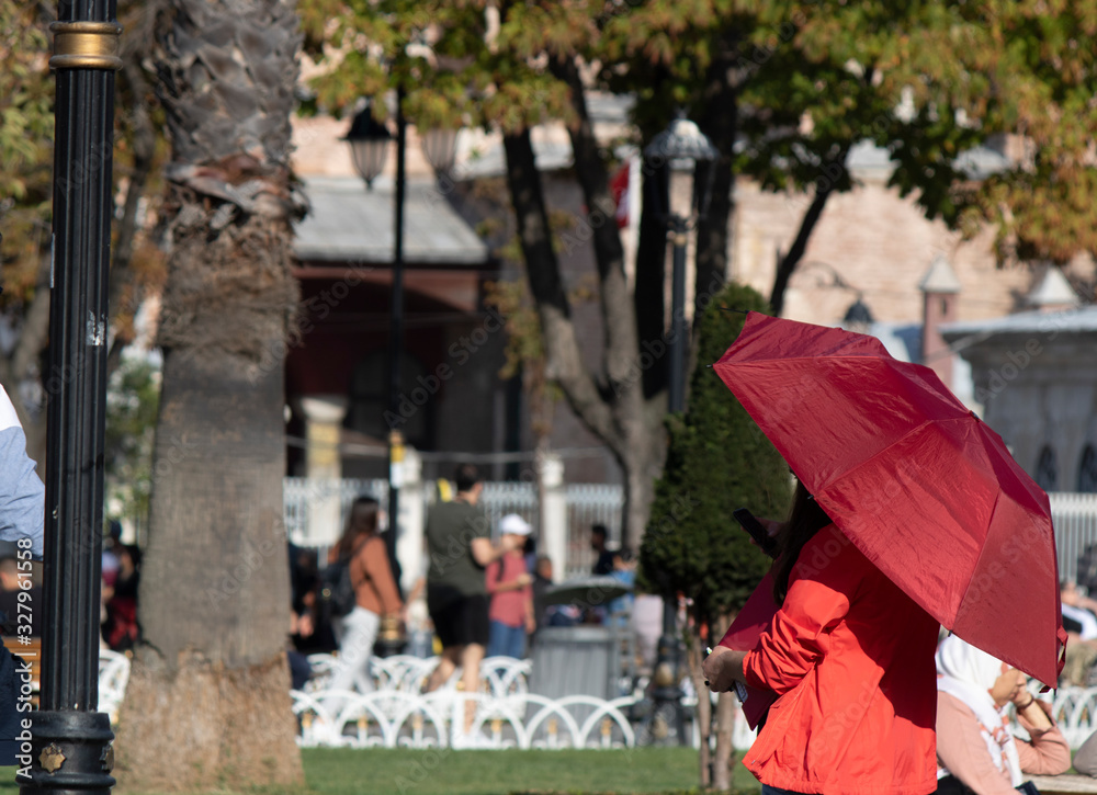 Woman with red umbrella in warm and sunny weather. Trying to be protected from the sun.