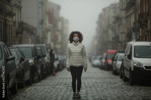 Asian woman in antiviral mask stands in the middle of a deserted street in foggy. photo