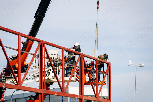 Professional welder with safety harness mounted on a crane and welding a metal structure
