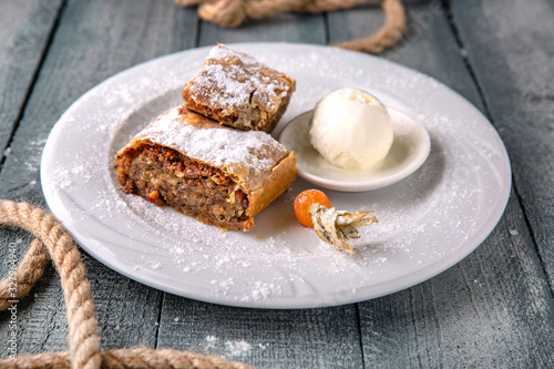 Apple strudel with caramel and nuts in icing sugar with a scoop of ice cream.
