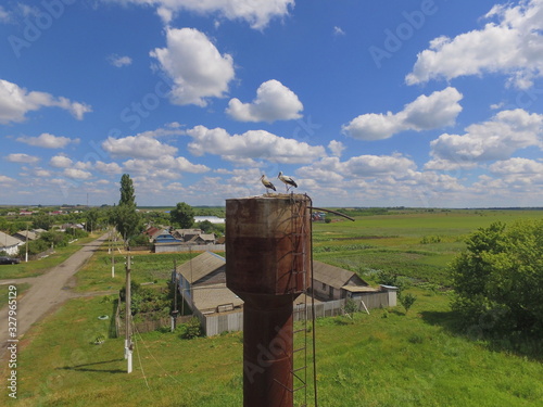 Storks on a water tower against a blue sky with many individual clouds, a village in Russia