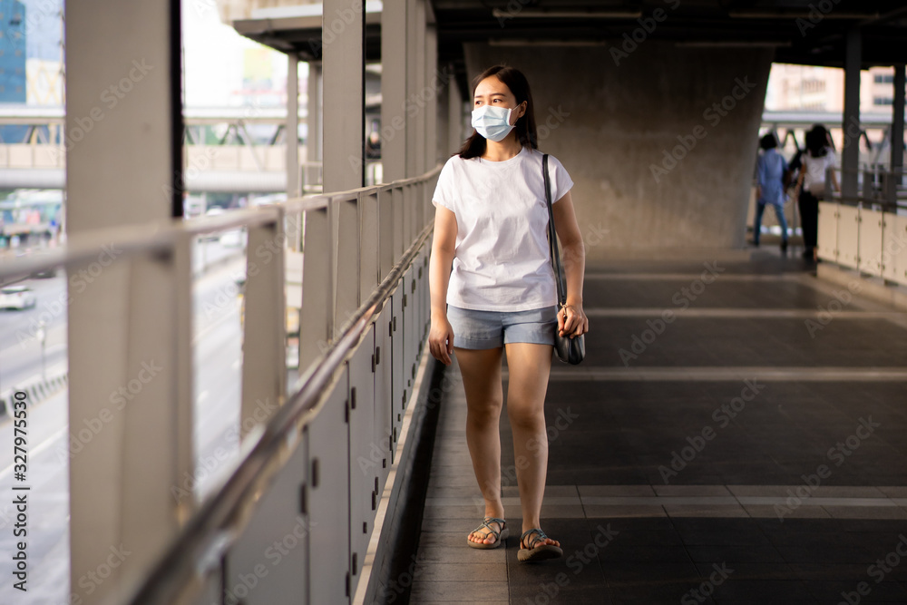 Asian woman standing beside the road in polluted city fully with pm2.5 dust. Woman wearing protective mask to protect herself from smog and pm2.5 dusty particle. Environment damaged from pollution.