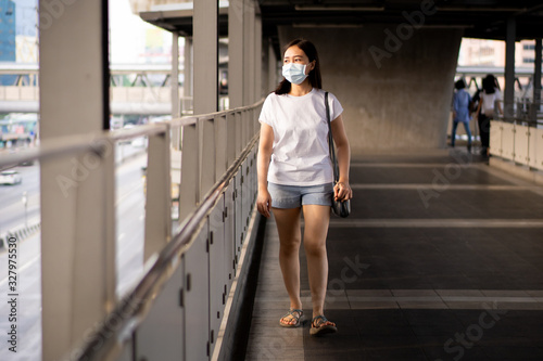 Asian woman standing beside the road in polluted city fully with pm2.5 dust. Woman wearing protective mask to protect herself from smog and pm2.5 dusty particle. Environment damaged from pollution.