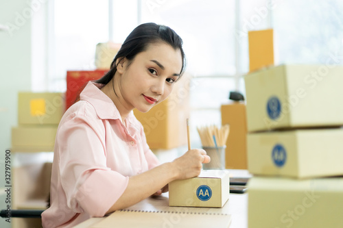 Young Asian business woman packing a post boxes to be shipped to customers. Ecommerce online shopping concept. Expertise online sales person packing customers parcel boxes for shipment.
