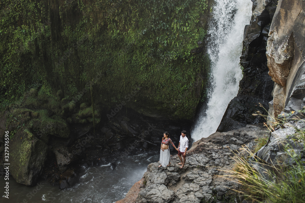 Couple travel in pregnancy. Amazing view of Tegenungan Bali cascade waterfall landscape. Morning sunlight, wanderlust concept