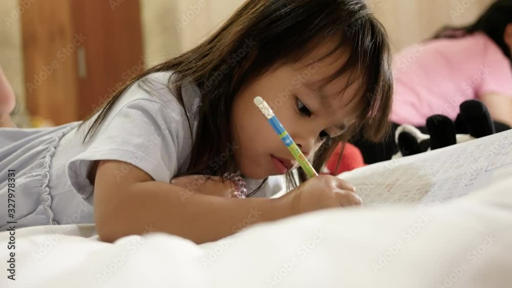 Cute little child girl doing her homework on bed at home. Cute little child girl doing her homework on bed at home.