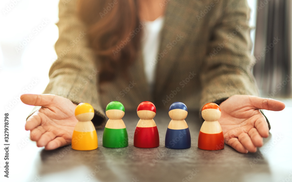 Closeup image of a woman showing a group of different colors wooden people toy in hands for diversity and business concept Closeup image of a woman showing a group of different colors wooden people toy in hands for diversity and business concept