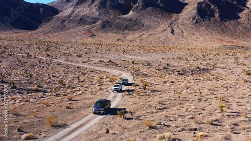 Professional drone videography shows a cinematic pullback of offroaders travelling on a dirt road in a desert landscape. photo