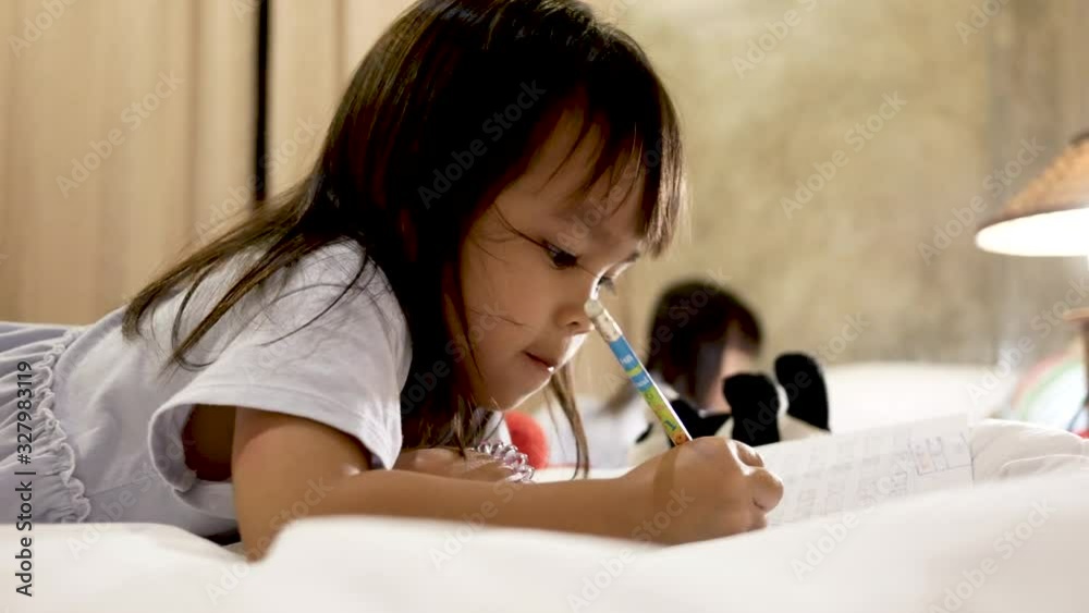 Cute little child girl doing her homework on bed at home. Cute little child girl doing her homework on bed at home.