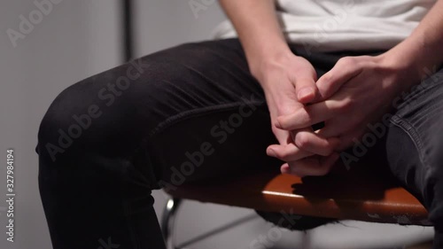 Closeup of the shaking legs and hands of a nervous or anxious man wearing black jeans and white shirt sitting on a chair