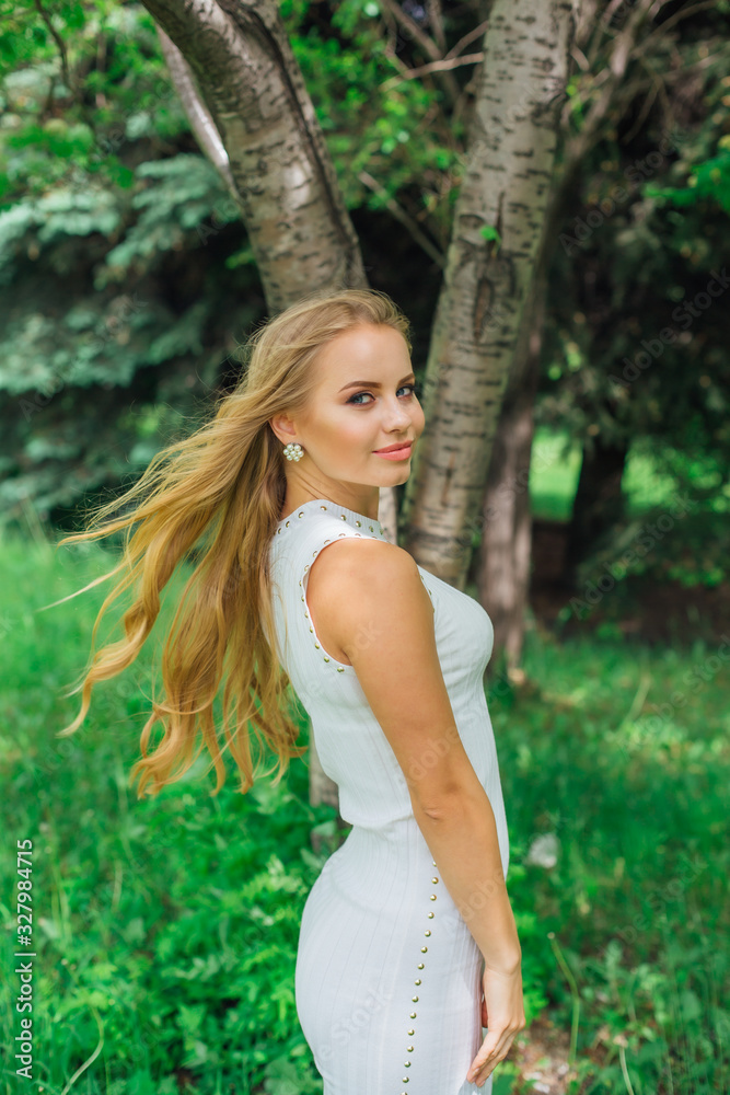 Naklejka premium Portrait of a charming blond woman wearing beautiful white dress standing next to rowan tree.