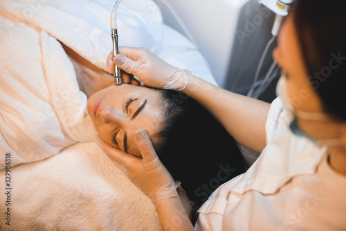 Charming caucasian brunette is having a facial spa procedure while lying with closed eyes