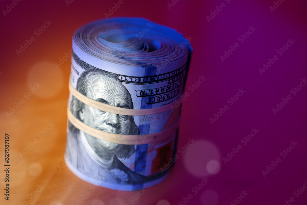 financial image of close up rolled and rubber banded American one hundred dollar bills pile on desk