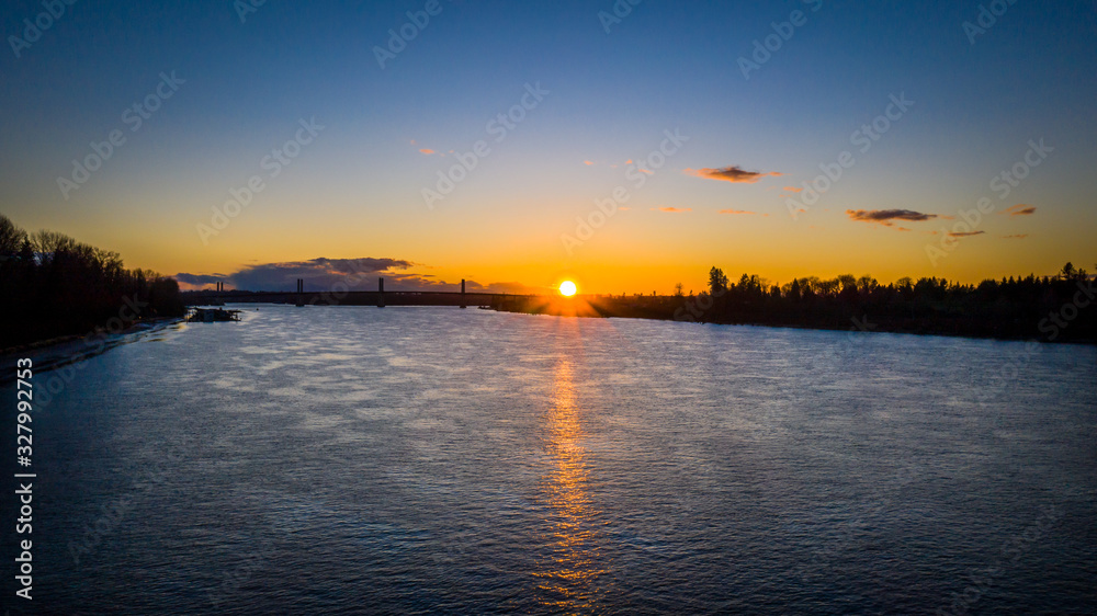 Aerial of sun setting over river bridge in the background