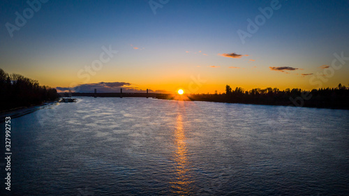 Aerial of sun setting over river bridge in the background