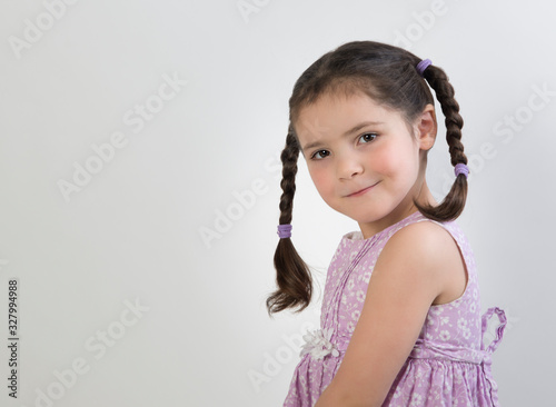 Preschool age girl in pink dress with cute expression and brown braids isolated on white background