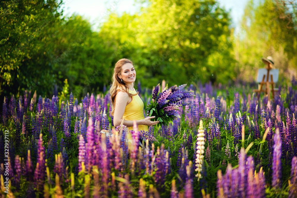 A girl artist in a yellow dress and hat draws a lupine field in the open air. Easel box with canvas, oil paint, palette and artist 's tools. A girl artist in a yellow dress and hat draws a lupine field in the open air. Easel box with canvas, oil paint, palette and artist 's tools.