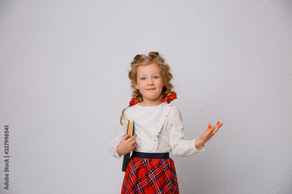 child girl in school uniform stands holding books in her hands shows emotions surprise, joy isolated on a white background child girl in school uniform stands holding books in her hands shows emotions surprise, joy isolated on a white background