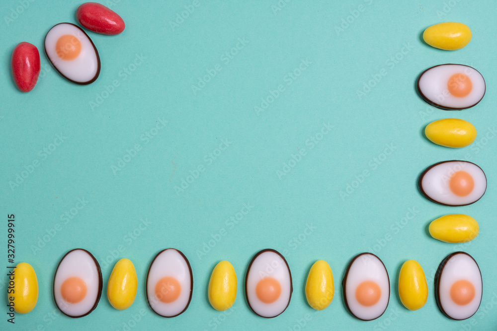 Little yellow Easter eggs arranged alternately in a line with Easter candies designed as egg white with yolk on an aqua menthe surface