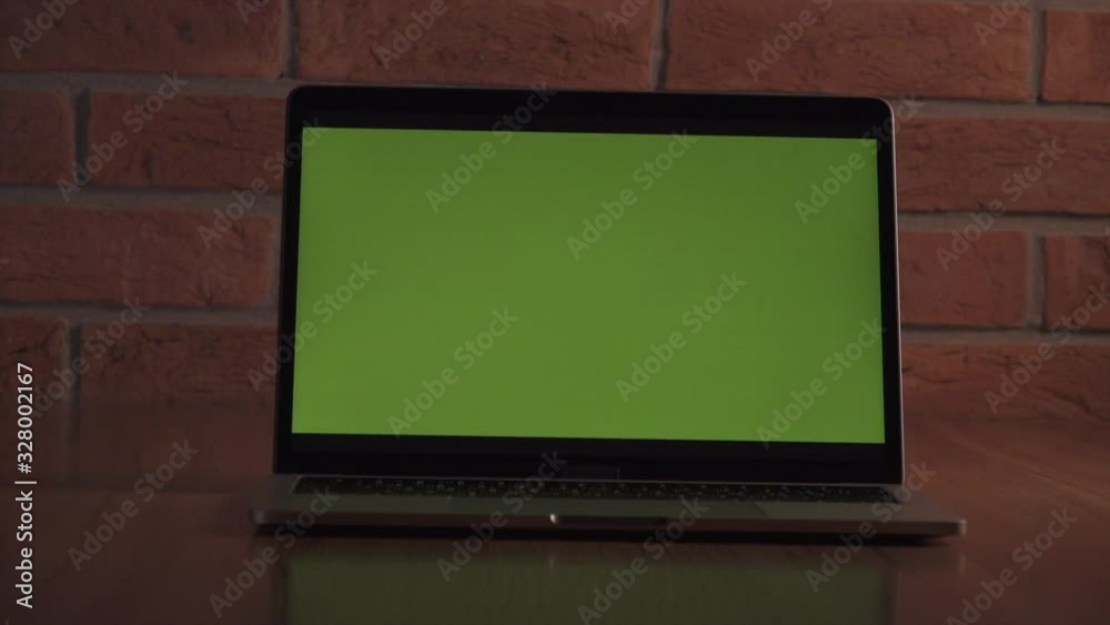 Green screen laptop for your content. Computer on  table in  office against  background of  brick wall. Camera moves.