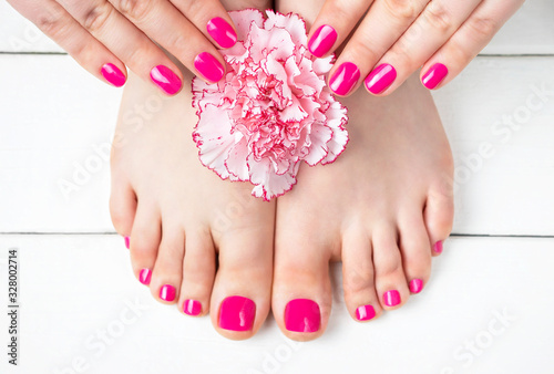 Pink manicure and pedicure with a flower on white wooden background, top view.