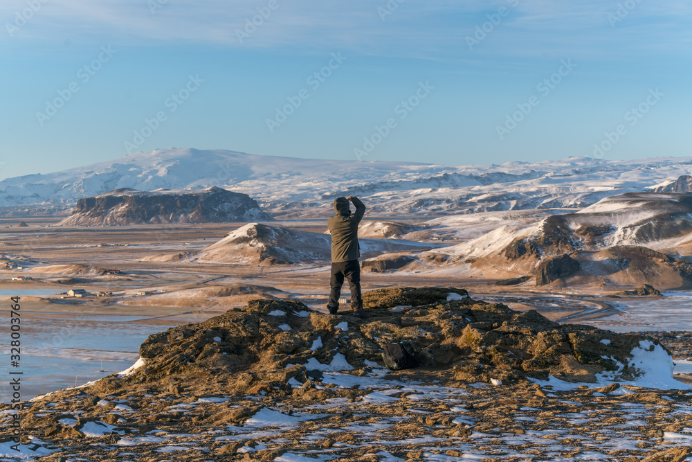 A man standing on the edge of mountain top taking photos and looking down at the natural landscapes of snow mountains in Iceland