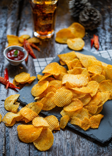 Potato chips spicy barbeque flavor on slate and wood floor with ketchup and soda drink for relaxation activity.