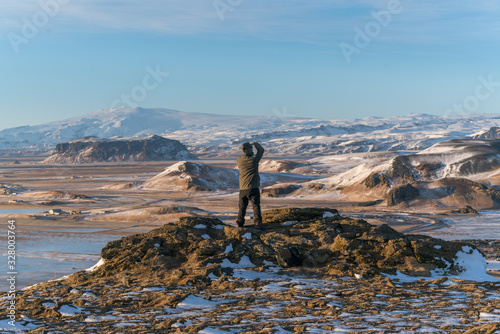 A man standing on the edge of mountain top taking photos and looking down at the natural landscapes of snow mountains in Iceland