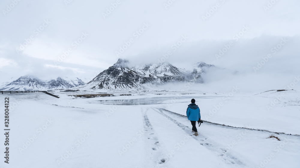 A man walking on the snow field with mountain at background, Iceland