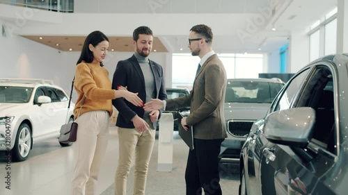 Slow motion of young couple man and woman buying car shaking hands with agent hugging taking keys enjoying successful deal. People and shopping concept.