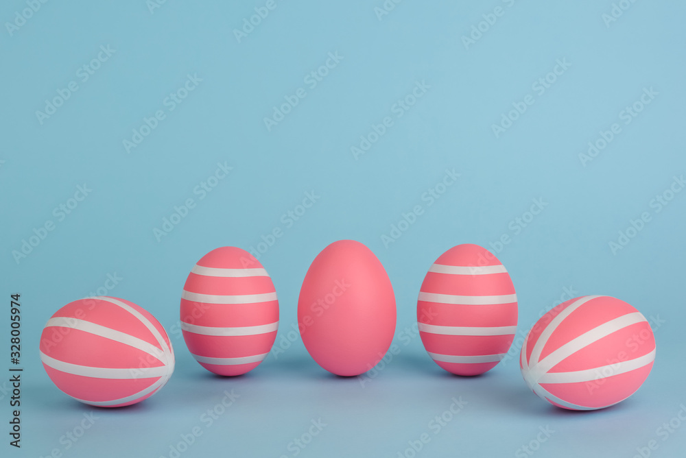 Easter decorated pink eggs. Five striped pink eggs in a row on a blue background. White stripes on pink painted eggs. Copy space. Happy Easter card. Colourful Easter concept.