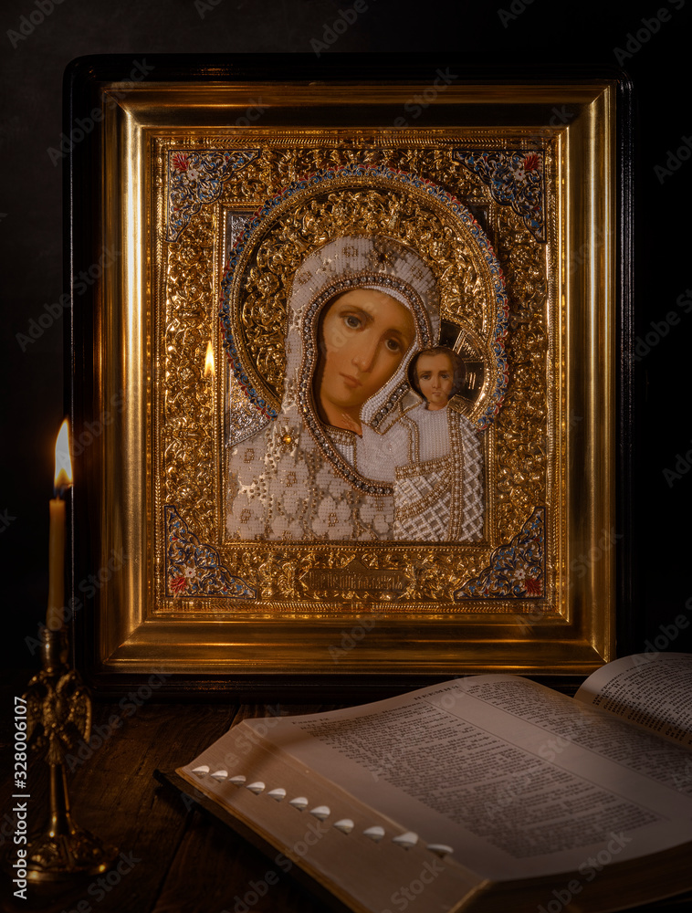 Icon of the Kazan mother of God  with a burning Church candle next to it.