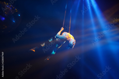 American strong sexy man do performance on aerial strap in blue lights. Sport training gym and lifestyle concept. Black background. Circus show in night club. Performance in night club.