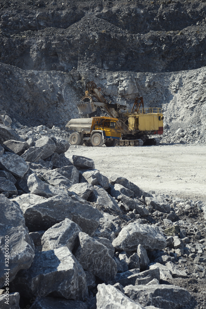 Mining excavator and mining truck in a quarry on the background of rocky terrain. Mining excavator and mining truck in a quarry on the background of rocky terrain.