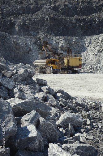 Mining excavator and mining truck in a quarry on the background of rocky terrain.