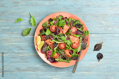 Salmon salad with cherry tomatoes, spinach, radicio, lollo on dish. Healthy seafood, salmon fish, creative diet concept. Tasty salmon and mixed leaves salad on blue wood, top view photo