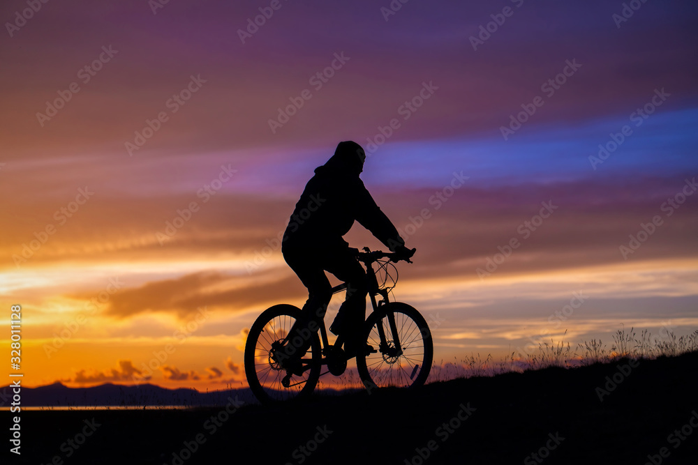 A cyclist rides in the mountains in the evening at sunset. Silhouette raider on a background of magnificent sunset A cyclist rides in the mountains in the evening at sunset. Silhouette raider on a background of magnificent sunset