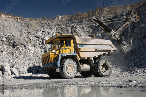 Large quarry dump truck on the background of a working excavator in a limestone quarry  close-up. Heavy equipment.